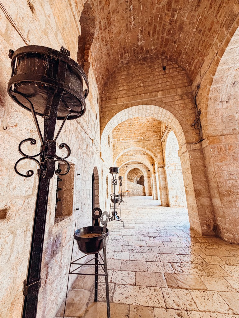 Stone corridor with arched ceilings and decorative metal stands.