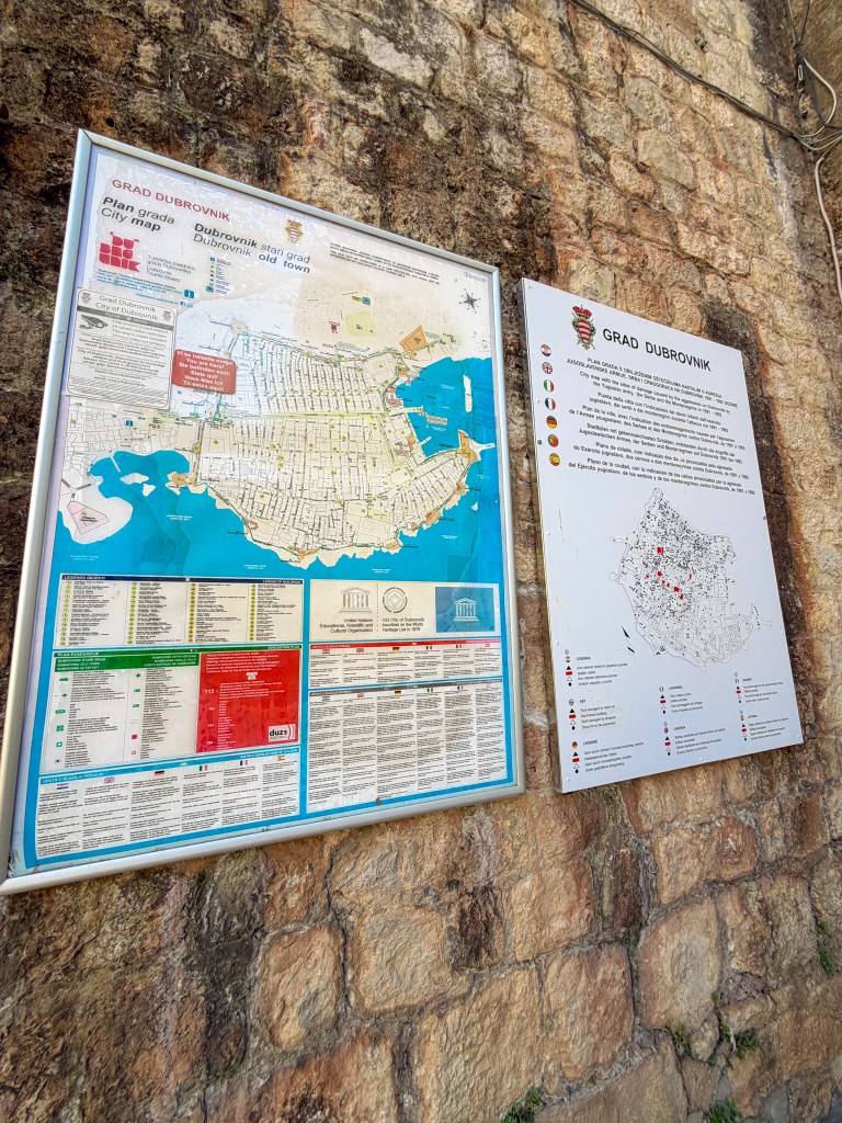 A city map of Dubrovnik displayed on a stone wall, showing the layout of the old town, key landmarks, and points of interest.