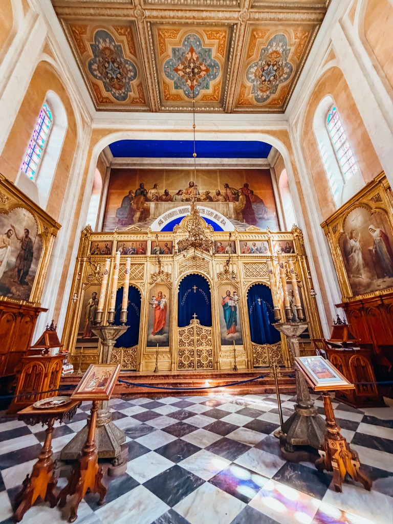 Interior view of a beautifully decorated church, featuring ornate architecture, colorful stained glass windows, and religious icons on display. The altar is adorned with intricate gold detailing and paintings of saints.