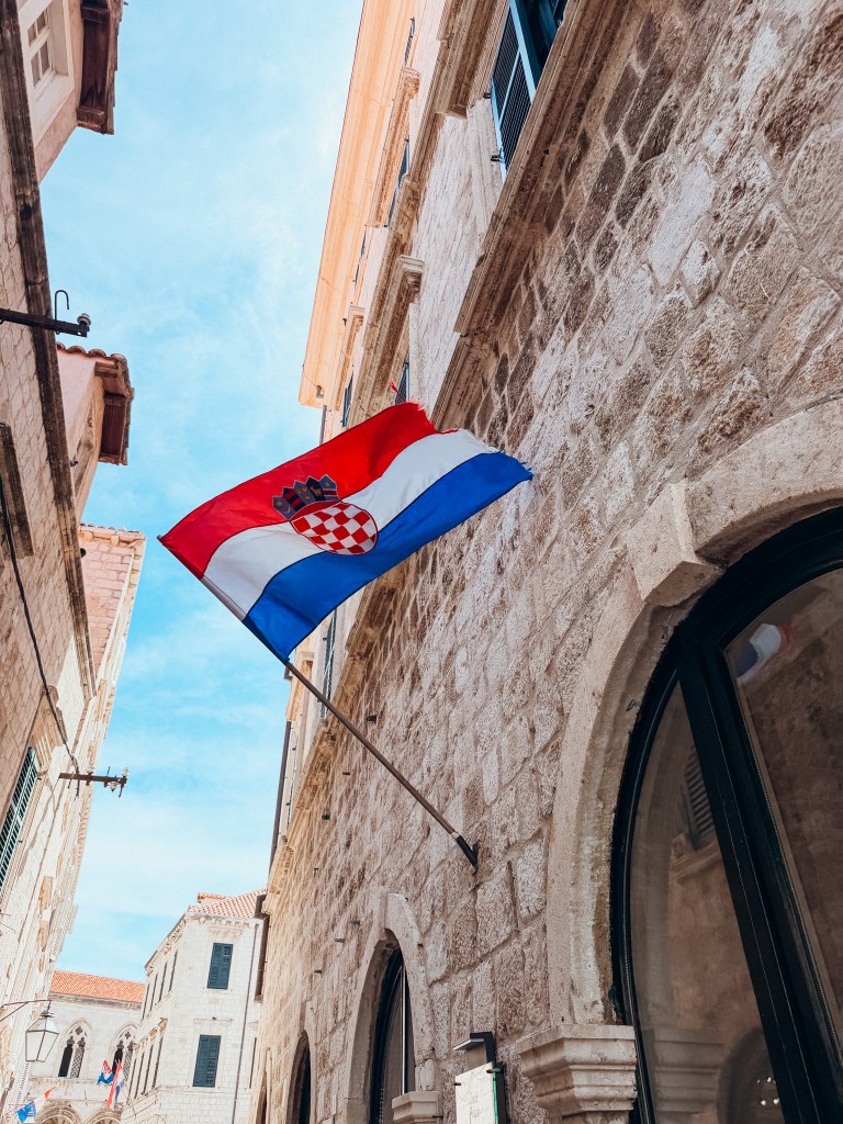 Croatian flag waving on a building in a narrow street with stone walls.